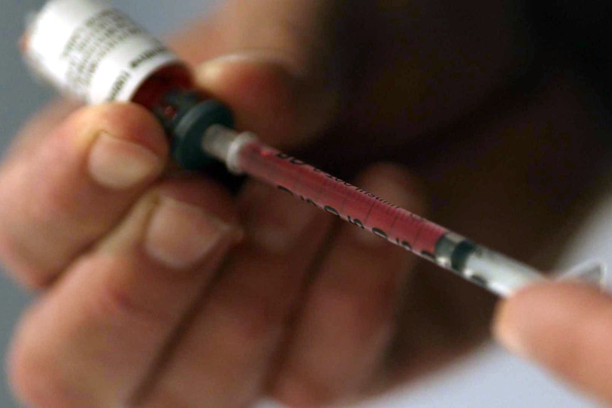 Close-up of hands drawing red liquid from a vial into a syringe.