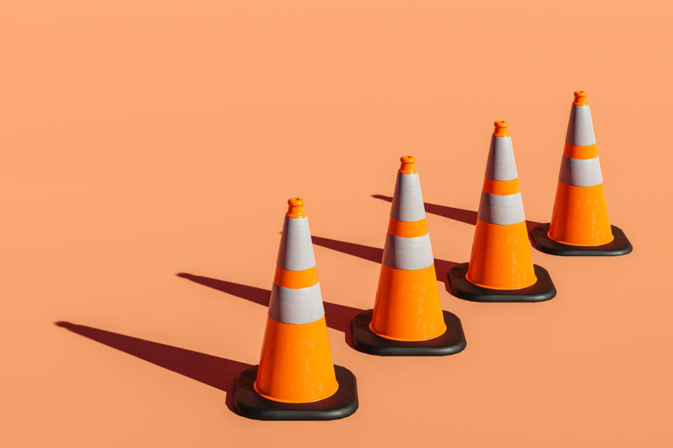 Four traffic cones in a row on a flat surface, casting shadows