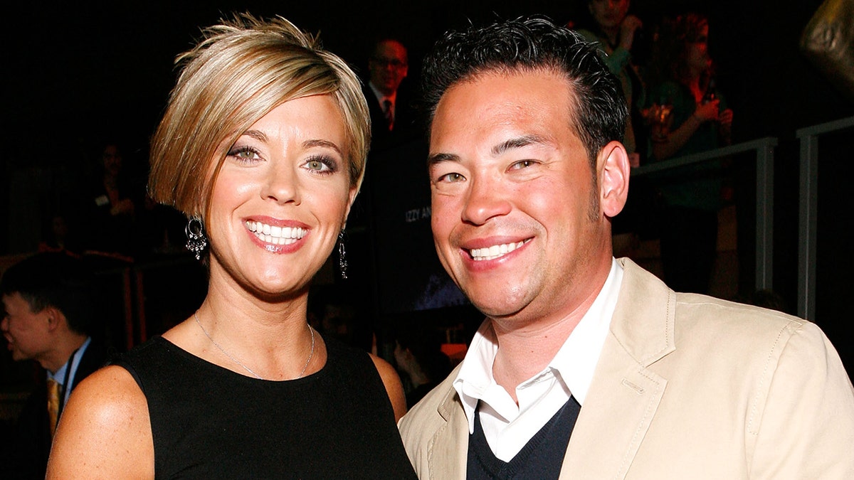 Kate Gosselin in a black dress with a short choppy haircut smiles next to Jon Gosselin in a brown blazer and dark sweater