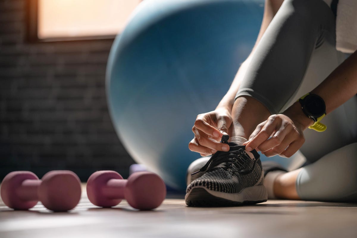 Person tying his shoe.  An exercise ball and two small dumbbells are nearby.