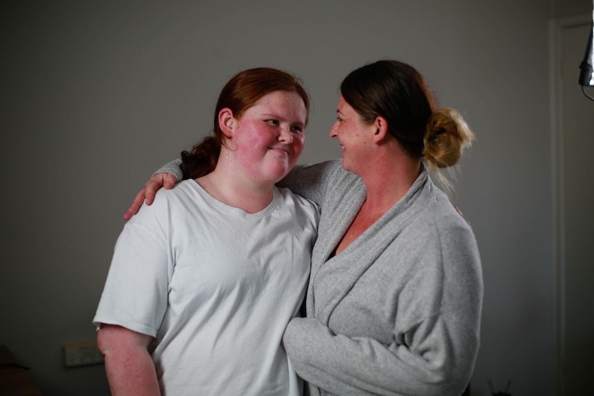 The mother smiles adorably with her arm around her daughter as they look into each other's eyes.