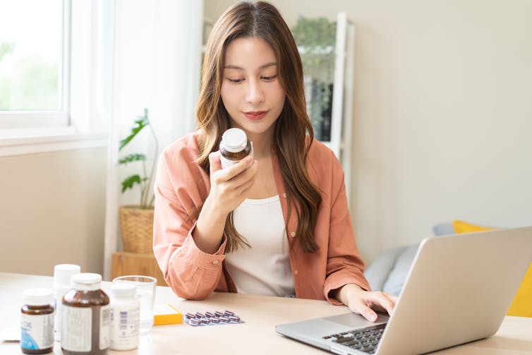 A woman reading a medicine label in front of a laptop computer